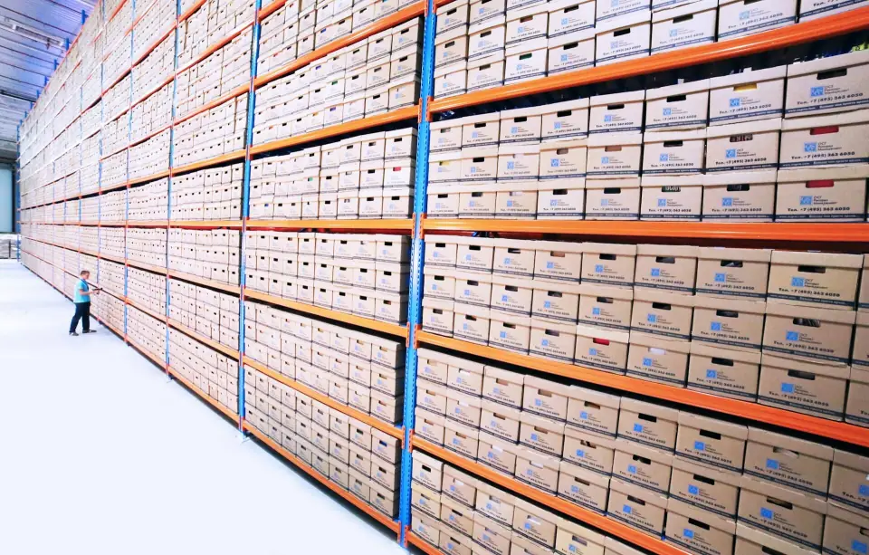Long rows of shelves with archive boxes and a tiny figure at the end of the aisle